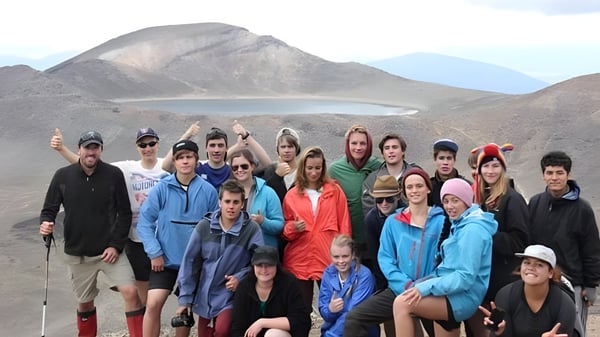 Eine Gruppe von Schülern der Freyberg High School posiert vor einer malerischen Berglandschaft mit See.