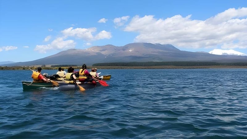 Schüler der Freyberg High School paddeln in einem kleinen Boot auf einem See vor einer Berglandschaft.