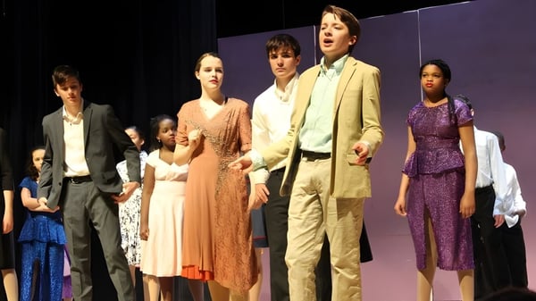 Eine Gruppe von Schülern der Friends School of Baltimore steht in formeller Kleidung auf einer Bühne mit violettem Hintergrund.