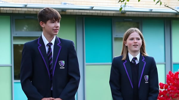Zwei Schülerinnen und Schüler in Schuluniformen stehen vor einem grünen Gebäude auf dem Campus des Frome College.