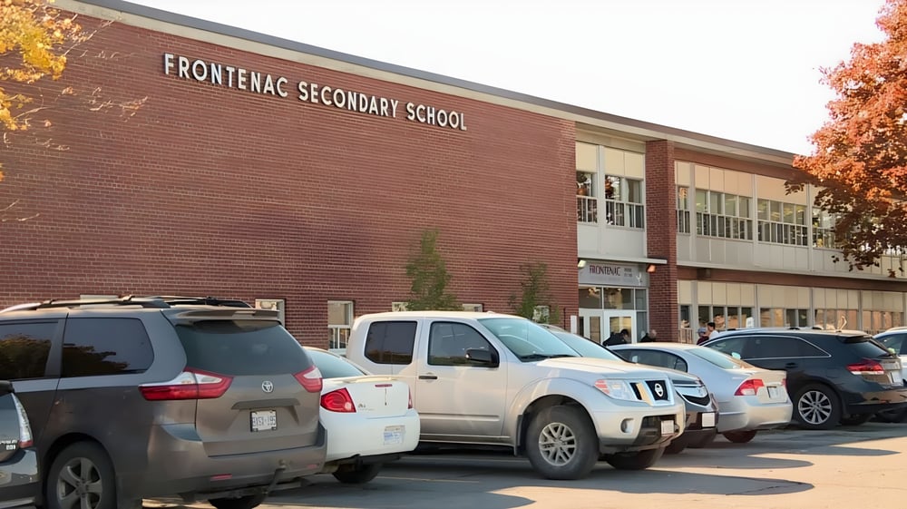 Das Backsteingebäude der Frontenac Secondary School mit mehreren geparkten Fahrzeugen im Vordergrund.