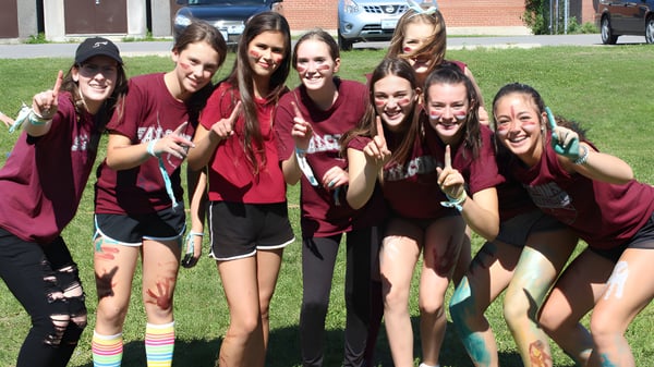 Eine Gruppe Schülerinnen in roten Shirts posiert auf dem Rasen vor einem Backsteingebäude der Frontenac Secondary School.