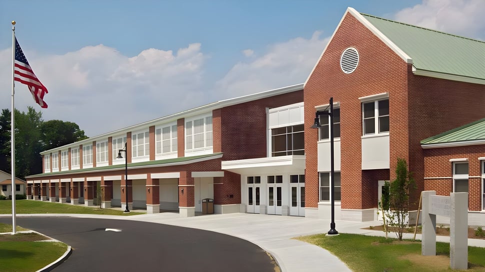 Das Backsteingebäude der Fryeburg Academy mit grünem Dach und amerikanischer Flagge im Vordergrund ist von einer Auffahrt und Rasenflächen umgeben.