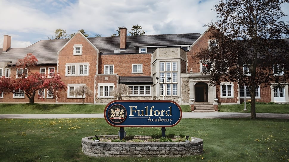 Das Backstein- und Steingebäude der Fulford Academy steht auf einem grünen Gelände mit Bäumen und ist von ähnlichen Gebäuden umgeben.