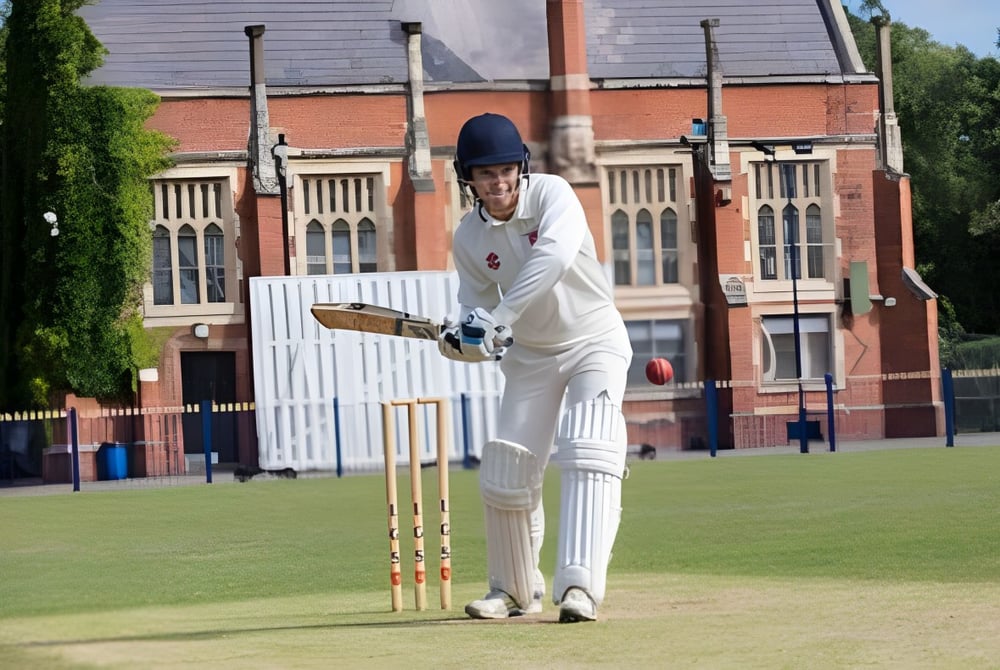 Ein Schüler der Fulneck School steht in Cricket-Ausrüstung auf einem Rasenfeld vor einem Backsteingebäude.
