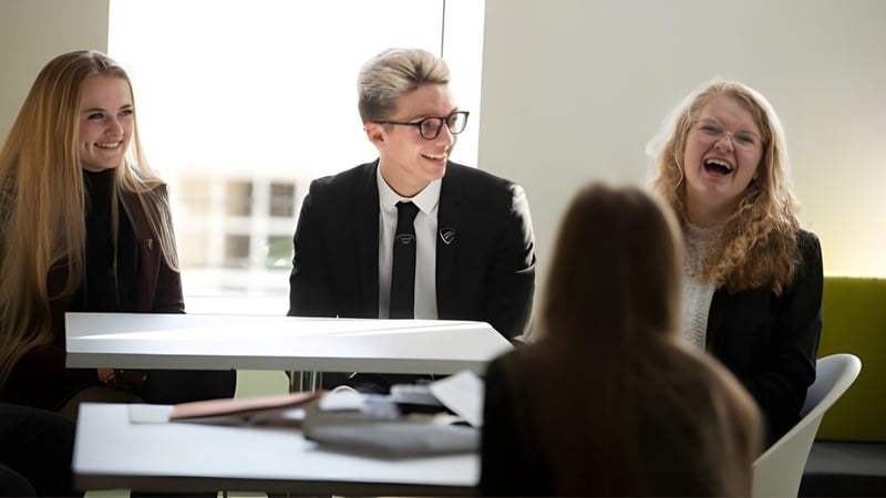 Drei Schüler der Fulneck School sitzen in formeller Kleidung an einem Tisch in einem modernen Besprechungsraum.