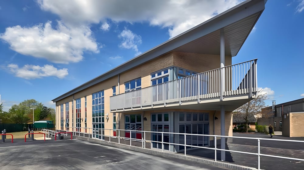 Das moderne mehrstöckige Schulgebäude der Fulston Manor School mit großen Fenstern und Balkon vor blauem Himmel.