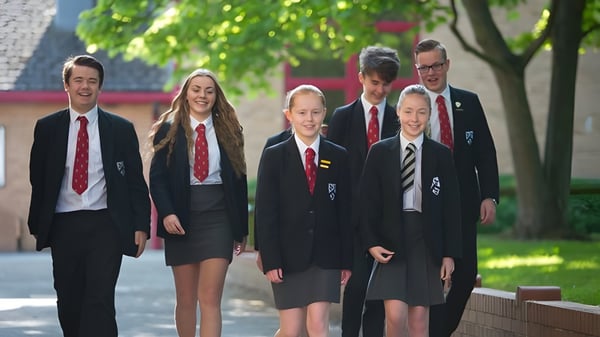 Eine Gruppe Schülerinnen und Schüler in Schuluniformen läuft gemeinsam auf dem Campus von Fulston Manor mit Bäumen und Gebäuden im Hintergrund.