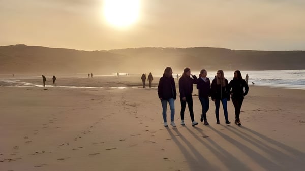 Eine Gruppe von Schülerinnen und Schülern der Fyling Hall School geht bei Sonnenuntergang am Strand entlang.