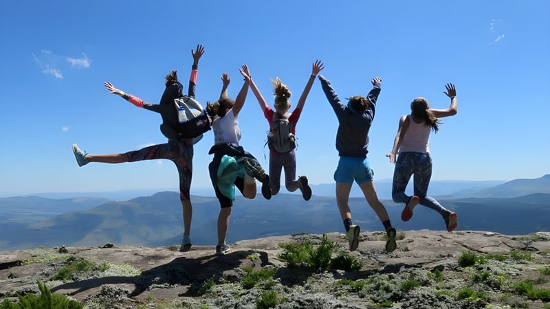 Eine Gruppe von Schülerinnen und Schülern des Galway Community College springt auf einem felsigen Vorsprung vor einer Berglandschaft.