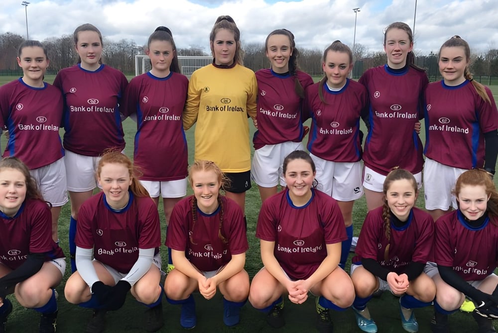 Eine Gruppe weiblicher Fußballspielerinnen posiert in den Vereinsfarben auf dem Sportplatz des Galway Community College.