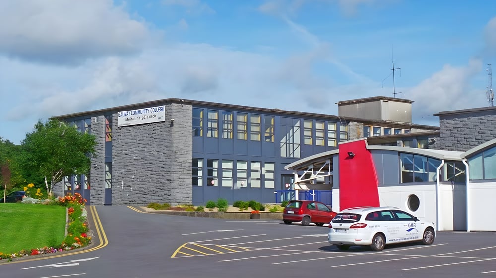 Das mehrstöckige, rot-weiße Gebäude des Galway Community College steht vor einem Parkplatz mit viel Grün im Hintergrund.