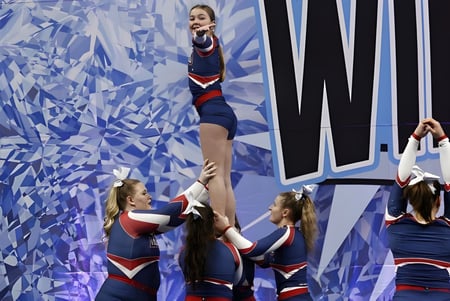 Schüler der Gananoque Secondary School führen einen akrobatischen Cheerleading-Stunt vor einem blauen abstrakten Hintergrund aus.