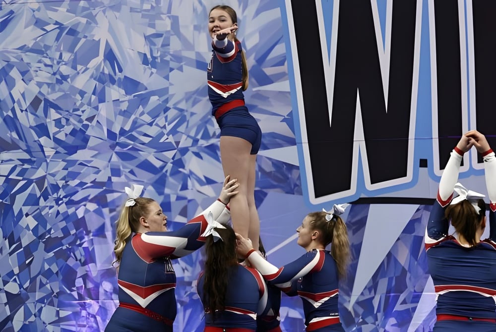 Schüler der Gananoque Secondary School führen einen akrobatischen Cheerleading-Stunt vor einem blauen abstrakten Hintergrund aus.
