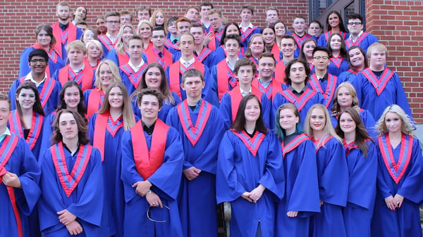 Eine große Gruppe von Absolventinnen und Absolventen der Gananoque Secondary School steht in blauen und roten Talaren vor einem Backsteingebäude.