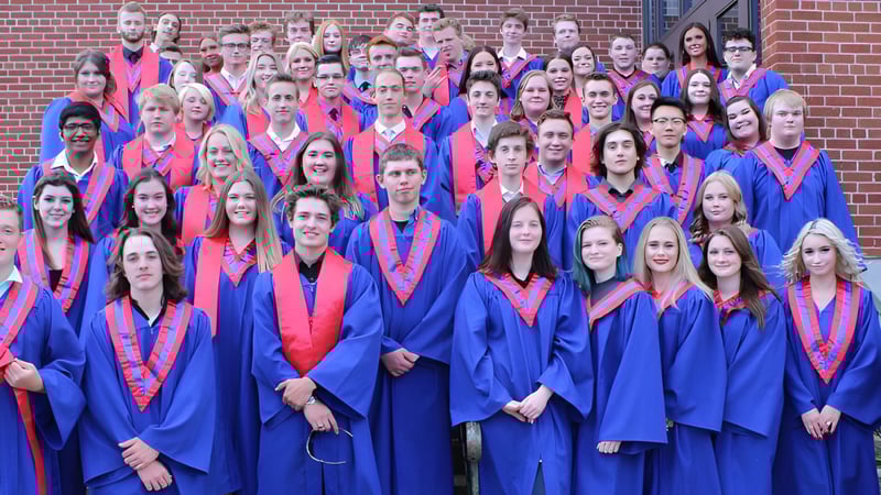 Eine große Gruppe von Absolventinnen und Absolventen der Gananoque Secondary School steht in blauen und roten Talaren vor einem Backsteingebäude.