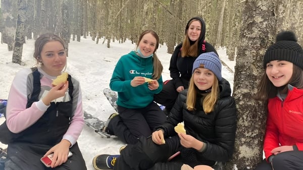 Eine Gruppe Schülerinnen des Gander Collegiate steht gemeinsam winterlich gekleidet in einem verschneiten Wald.