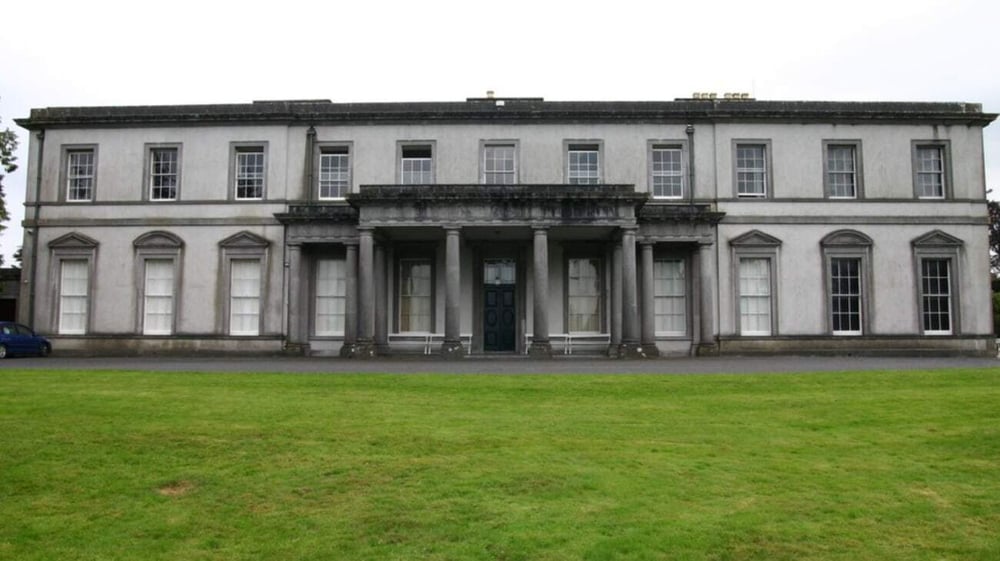 Das neoklassizistische Hauptgebäude des Garbally College steht auf einem Rasen mit Bäumen im Hintergrund.