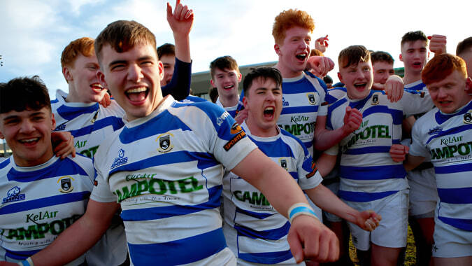 Eine Gruppe junger Rugbyspieler feiert ihren Sieg auf dem Spielfeld des Garbally College vor bewölktem Himmel.