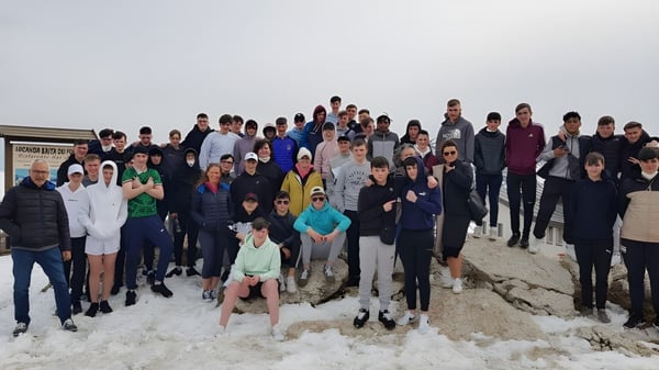 Eine große Gruppe von Menschen steht bei Garbally College gemeinsam auf einer verschneiten Landschaft unter bewölktem Himmel.