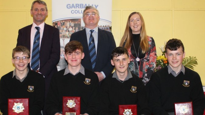 Schüler und Lehrer des Garbally College posieren gemeinsam für ein Gruppenfoto vor einem Banner der Schule.