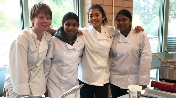 Vier Schüler der Garibaldi Secondary School stehen gemeinsam in einer Schulküche in Kochuniformen.