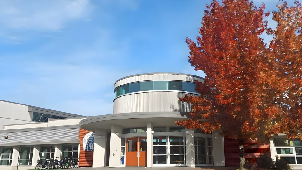Das moderne Gebäude der Garibaldi Secondary School mit Glaswänden steht vor roten Herbstbäumen unter blauem Himmel.