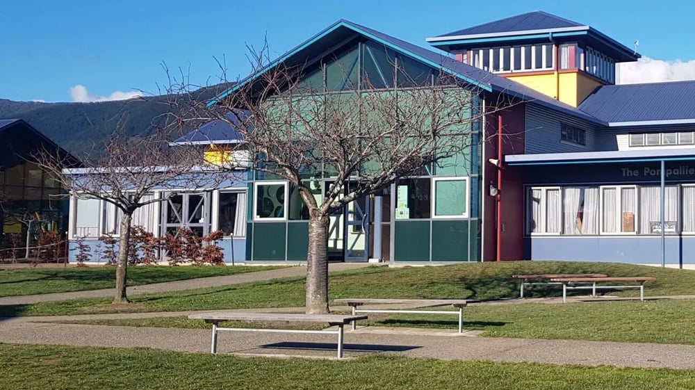 Das moderne und farbenfrohe Gebäude des Garin College ist von einer Grünfläche mit Bänken und Bäumen umgeben.