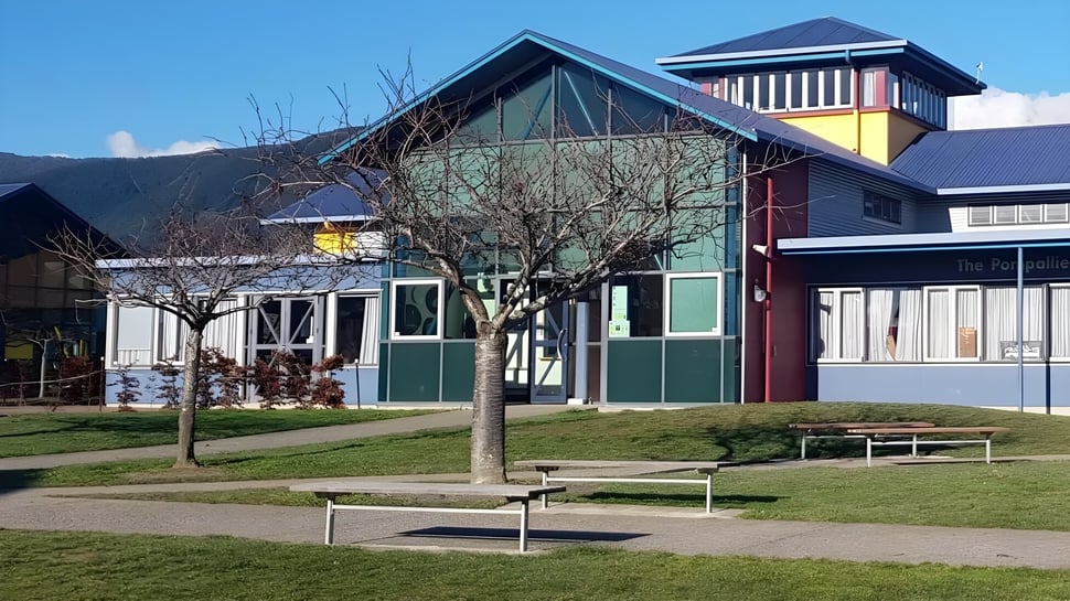 Das moderne Garin College Gebäude mit markantem Dach steht auf einer Grünfläche mit Bänken und Bäumen unter blauem Himmel.
