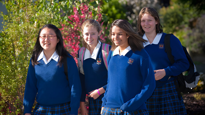 Vier Schülerinnen im Schuluniform stehen gemeinsam in einem Garten auf dem Campus des Garin College.