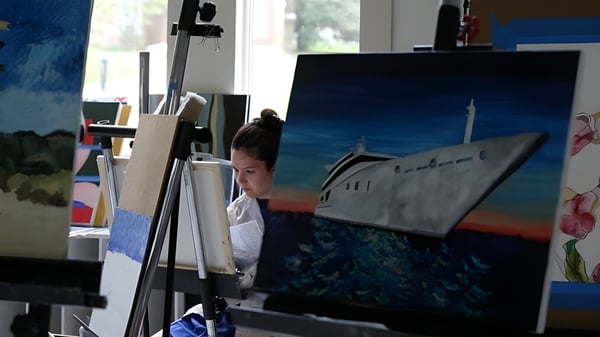 Ein Schüler malt auf einer Staffelei im Kunstunterricht der Garrison Forest School mit Kunstmaterialien im Raum.