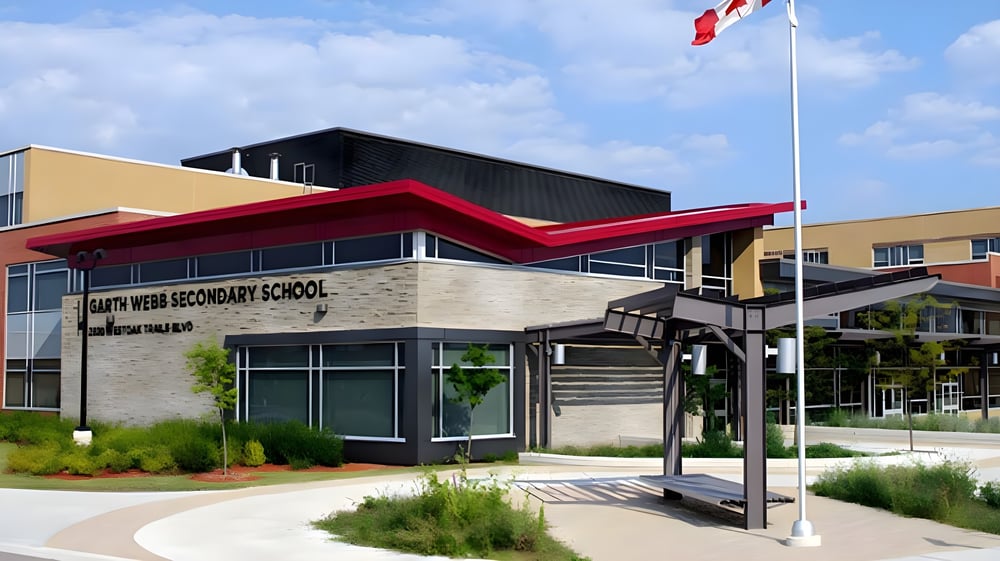Das moderne mehrstöckige Gebäude der Garth Webb Secondary School mit rotem Vordach und kanadischer Flagge davor.