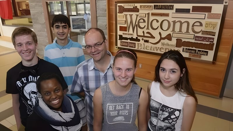 Eine Gruppe Schülerinnen und Schüler steht vor einem Willkommensschild auf dem Campus der Garth Webb Secondary School.