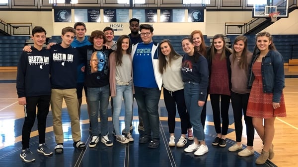 Eine Gruppe Schülerinnen und Schüler steht in der Sporthalle der Gaston Day School mit mehreren Sportbannern im Hintergrund.