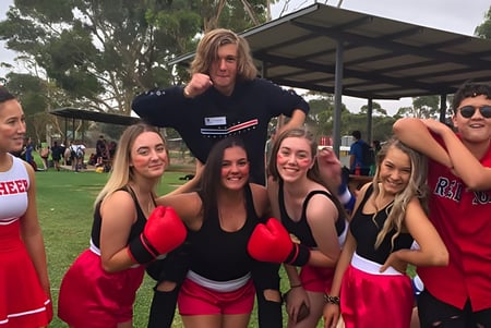 Eine Gruppe Schülerinnen und Schüler der Gawler and District College posiert gemeinsam im Freien in einem parkähnlichen Bereich, einige tragen Cheerleader-Uniformen.