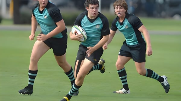 Drei Rugbyspieler der Geelong Grammar School laufen mit Ball über ein grünes Spielfeld.