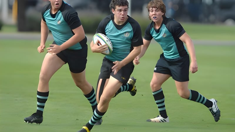 Drei Rugbyspieler der Geelong Grammar School laufen mit Ball über ein grünes Spielfeld.