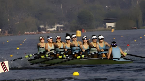 Eine Gruppe von Schülerinnen und Schülern der Geelong Grammar School rudert auf einem Gewässer vor bewaldeter Kulisse.
