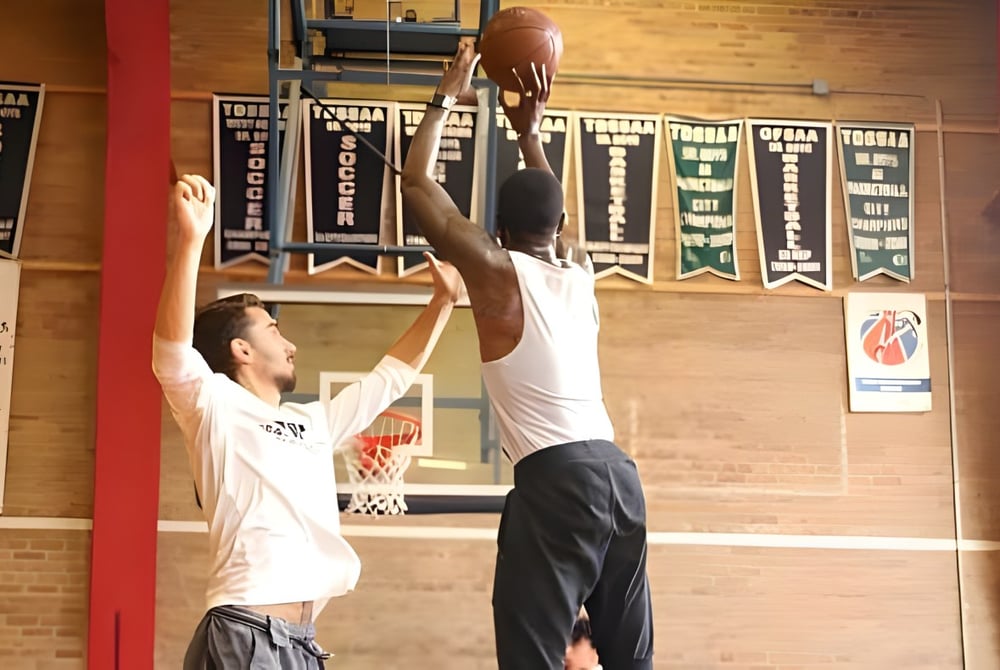 Zwei Schülerinnen und Schüler der George Harvey Collegiate Institute spielen Basketball in einer Turnhalle mit Sportbannern im Hintergrund.