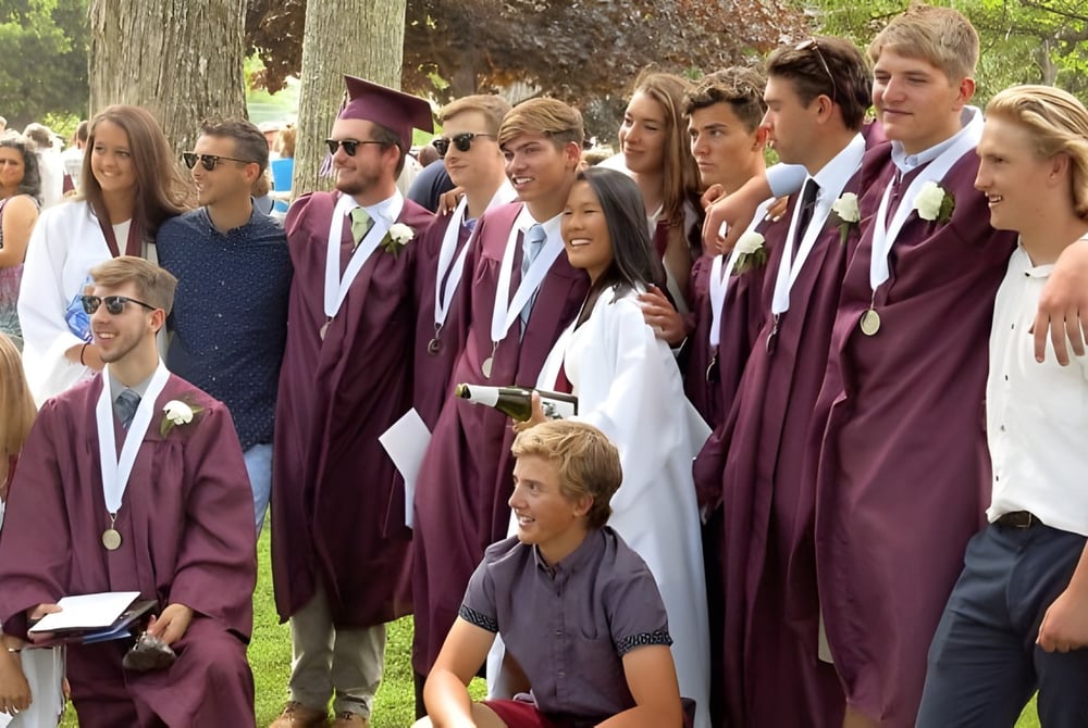 Eine Gruppe von Absolventinnen und Absolventen der George Stevens Academy steht in Burgunderroben im Wald.