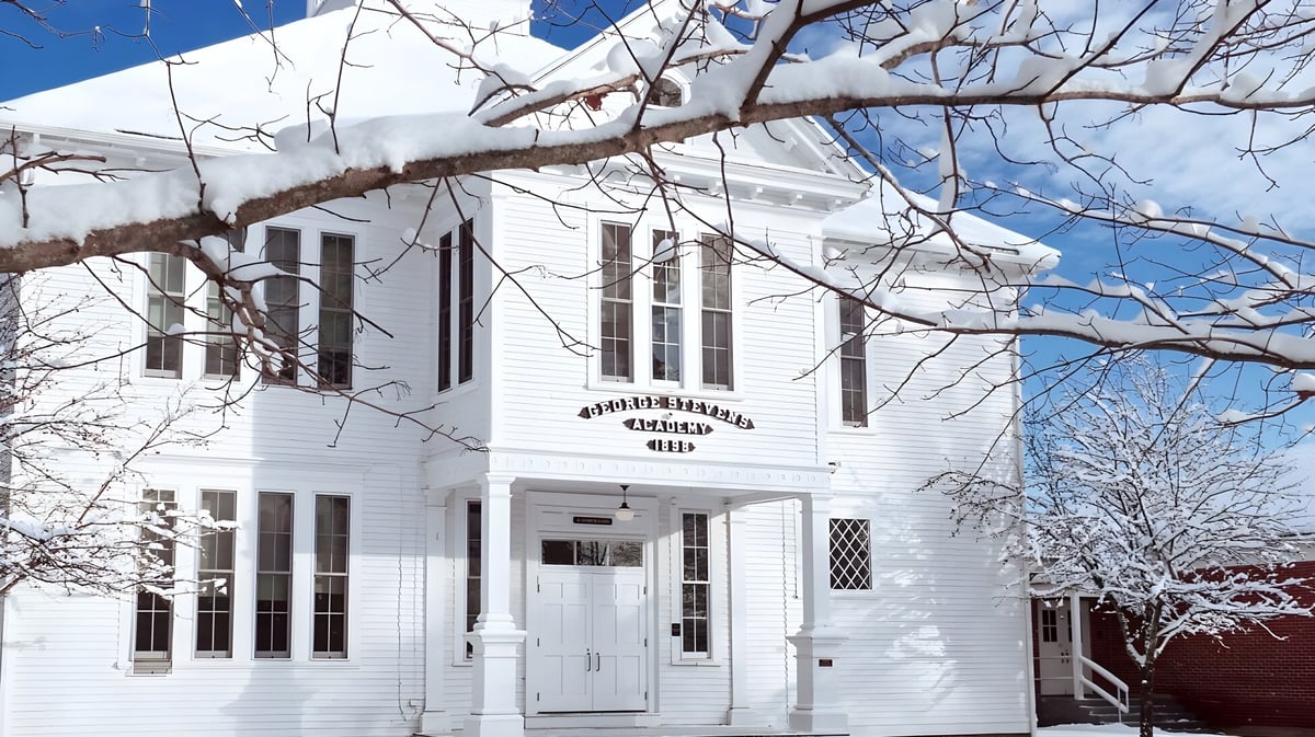 Das Gebäude der George Stevens Academy ist schneebedeckt und von kahlen Baumzweigen umgeben.