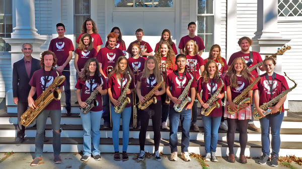 Schülerinnen der George Stevens Academy stehen in roten Uniformen mit Musikinstrumenten auf der Treppe eines Gebäudes mit Säulen.