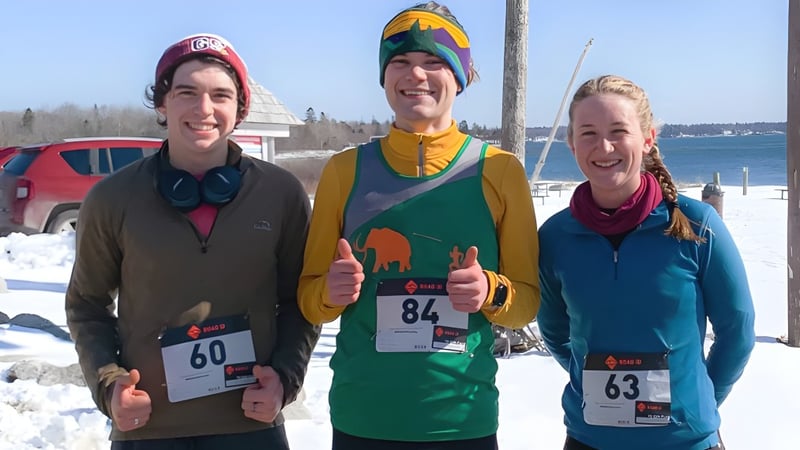 Drei Personen in Winterkleidung posieren vor einer verschneiten Landschaft auf dem Campus der George Stevens Academy.