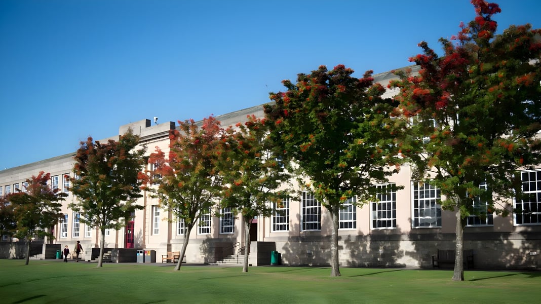Das Gelände von George Watson’s College zeigt einen grasbewachsenen Rasen und Gebäude vor herbstlich gefärbten Bäumen.
