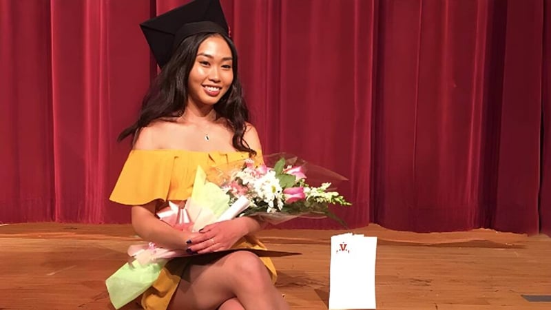 Eine Absolventin der Georges Vanier Secondary School steht vor einem roten Vorhang und hält einen Blumenstrauß in der Hand.