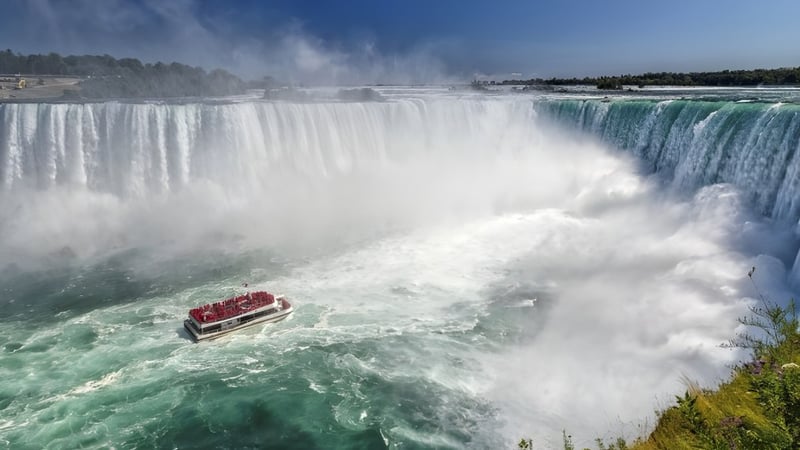 Ein Boot mit Passagieren fährt vor einem Wasserfall in der Nähe der Georgetown District High School.