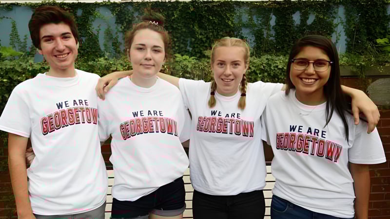 Vier Schüler der Georgetown District High School stehen zusammen vor einem grünen Heckenhintergrund und tragen weiße T-Shirts mit dem Aufdruck We are Georgetown.
