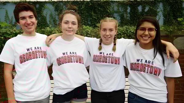 Vier Schüler der Georgetown District High School stehen zusammen vor einem grünen Heckenhintergrund und tragen weiße T-Shirts mit dem Aufdruck We are Georgetown.