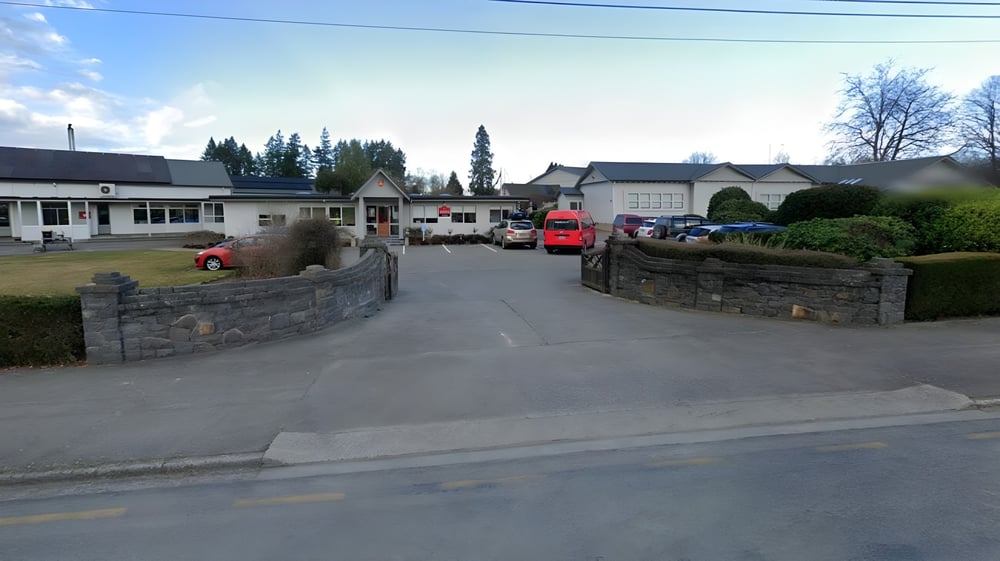 Eine Straße mit historischen Gebäuden und geparkten Autos neben der Geraldine High School vor einem Hintergrund aus Kiefern und blauem Himmel.