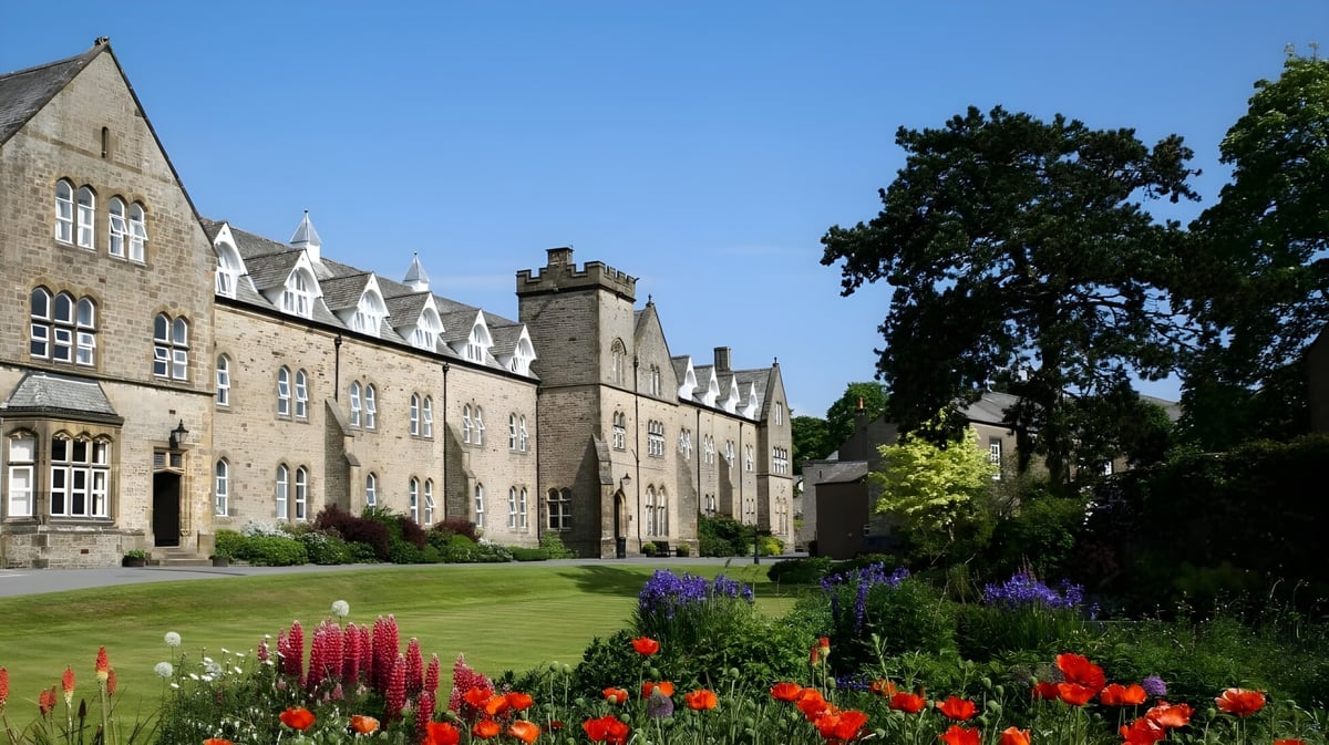 Das mittelalterlich anmutende Gebäude der Giggleswick School ist von einem blühenden Garten mit grüner Vegetation umgeben.